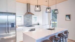 A modern kitchen with a large island, stainless steel appliances, and pendant lighting. - Paradise Lights 1770 (Seventeen Seventy)