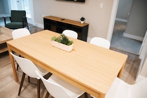 A dining area with a wooden table, white chairs, a small plant, and a black console table. - Downtown Houston Skyline Stay, Steps to Daikin Park C (Houston)