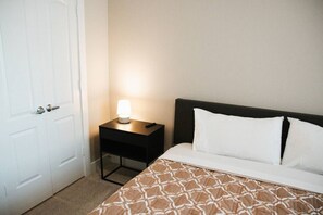 A hotel room with a bed, a bedside table with a lamp, and a white door. - Downtown Houston Skyline Stay, Steps to Daikin Park C (Houston)