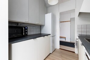 A compact kitchen with white cabinets, a black countertop, a microwave, a refrigerator, and a wooden bench.