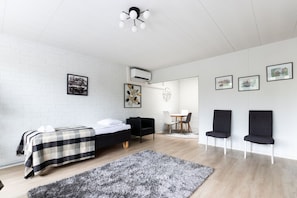 A modern hotel room with a bed, a black sofa, two chairs, a dining table, and artwork on the walls.
