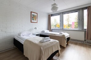 A hotel room with two beds, a white brick wall, a window with a view, and a ceiling light fixture. - Spacious and cozy 2-room apartment for 4 – Kaivoksela, Vantaa (Vantaa)