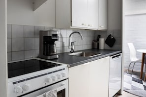 Een functionele keuken met een ingebouwd fornuis, een koffiezetapparaat, een spoelbak en witte keukenkastjes.