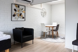 Een moderne kamer met een bed, een zwarte fauteuil, een eettafel met stoelen en een witte bakstenen muur.