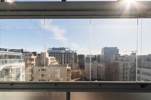 A cityscape through a window with multiple buildings, including a high-rise and a construction crane in the distance. - 3 bedroom family apartment with sauna and parking (Helsinki)