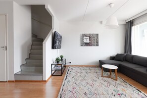 Ein modernes Wohnzimmer mit Treppe, Flachbildfernseher, Sofa, Couchtisch und einem gemusterten Teppich.