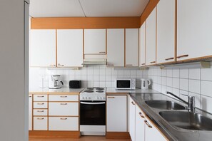 Une cuisine avec des meubles blancs, une cuisinière, un four à micro-ondes, une bouilloire et un évier.