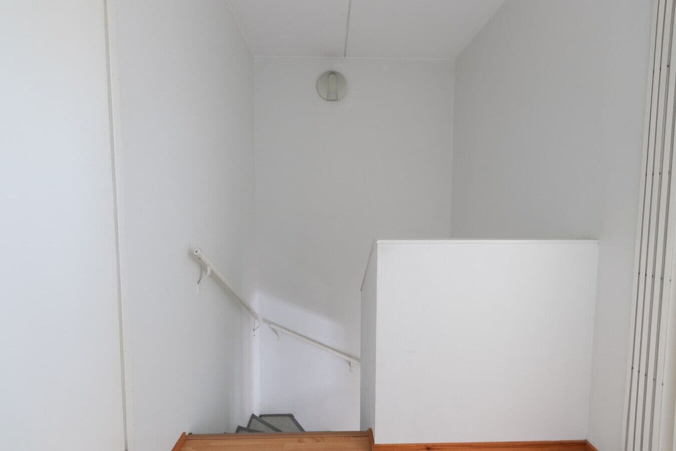 Een kamer met een witte wand, een houten vloer, een witte radiator en een wit kastje.