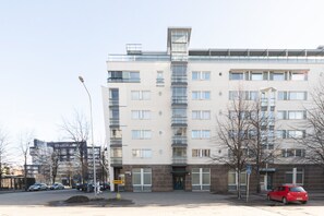 Ein mehrstöckiges Gebäude mit einer zentralen Treppe, einem Eingang im Erdgeschoss und einem Parkplatz mit Autos.