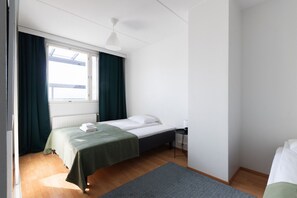 A single-bed room with a window, a radiator, a bedside table, and a desk. - 3 bedroom family apartment with sauna and parking (Helsinki)