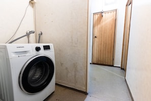 A laundry room with a Samsung digital inverter washing machine, a wooden door, and a concrete floor. - Functional and cozy 3 bedroom apartment for 6 (Vantaa)
