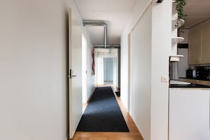 A narrow hallway with a dark carpet, white walls, and a wooden floor leading to a room with a door.