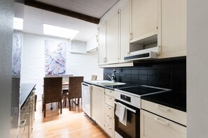 A modern kitchen with white cabinetry, a black countertop, and a dining area with wicker chairs.
