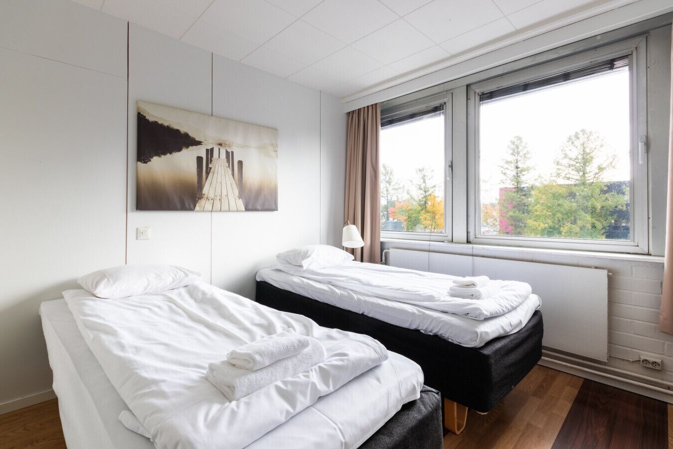 A hotel room with two beds, a window with a view of trees, and a painting on the wall.