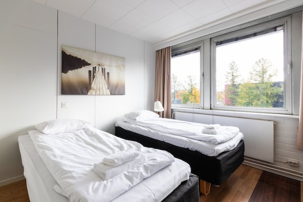 A hotel room with two beds, a window with a view of trees, and a painting on the wall.