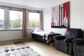A bedroom with a bed, a chair, a window with curtains, a painting, and a rug.