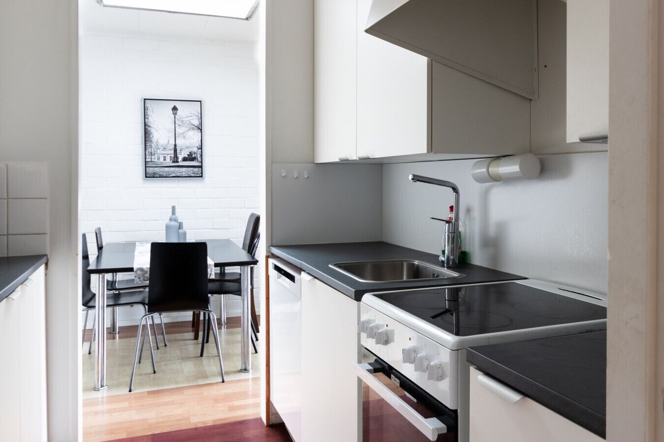 Une cuisine de taille réduite comprenant un évier, une cuisinière et un coin repas avec des chaises et une table.
