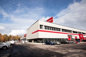 A commercial building with a red and white facade, multiple parking spaces, and a clear sky. - Spacious and cozy 2 bedroom apartment for 7 (Vantaa)