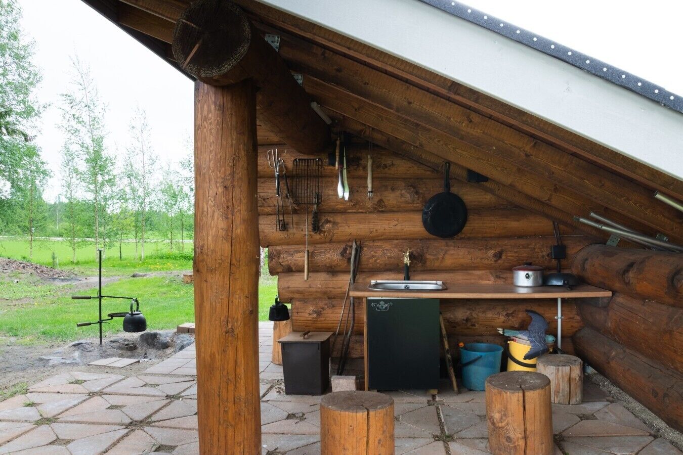 A rustic wooden cabin with a kitchen area, including a sink, stove, and hanging utensils.