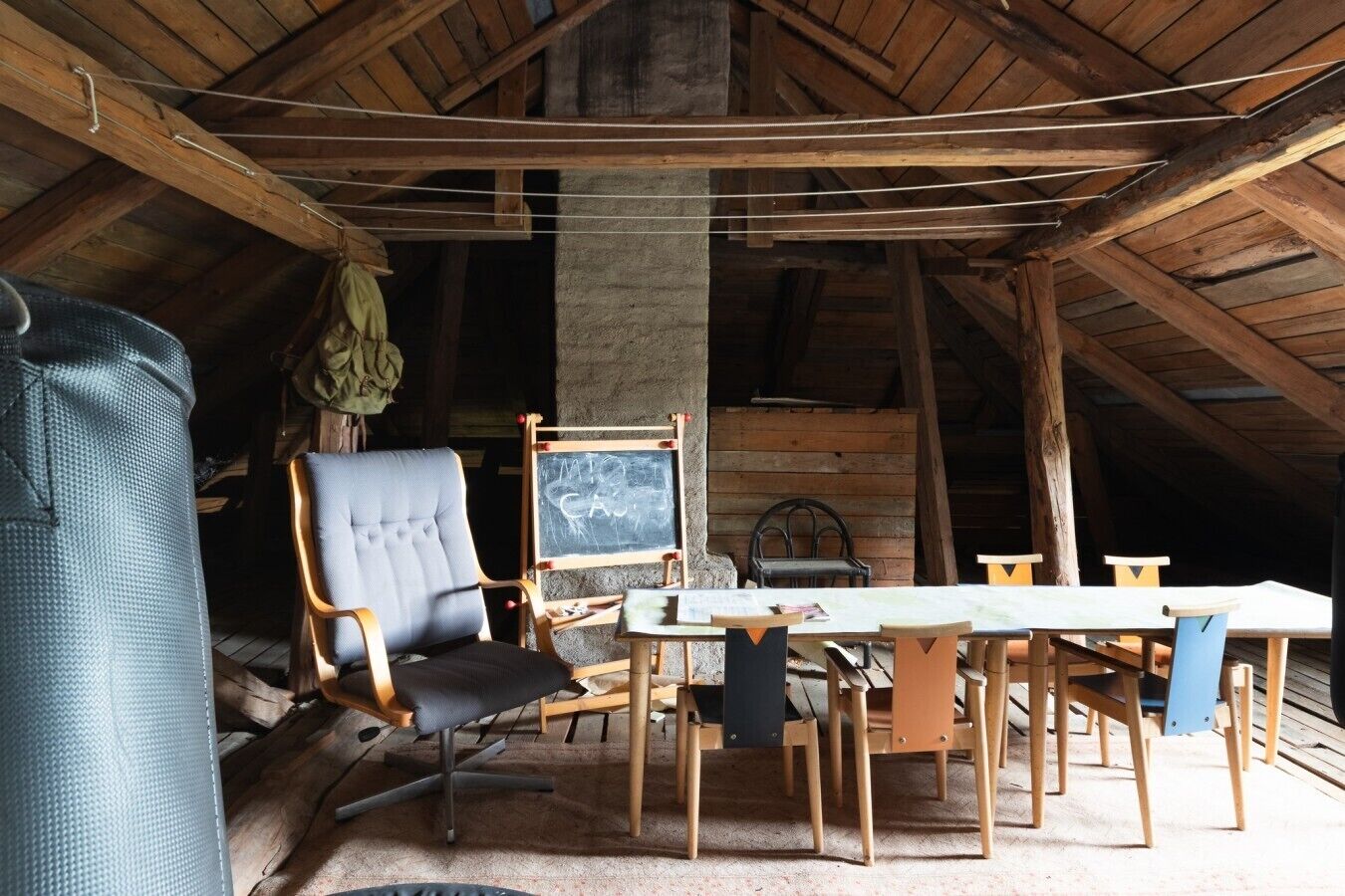 Una habitación rústica de madera con techo alto, una silla grande, una mesa y una pizarra.