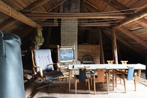A rustic wooden room with a high ceiling, a large chair, a table, and a chalkboard.