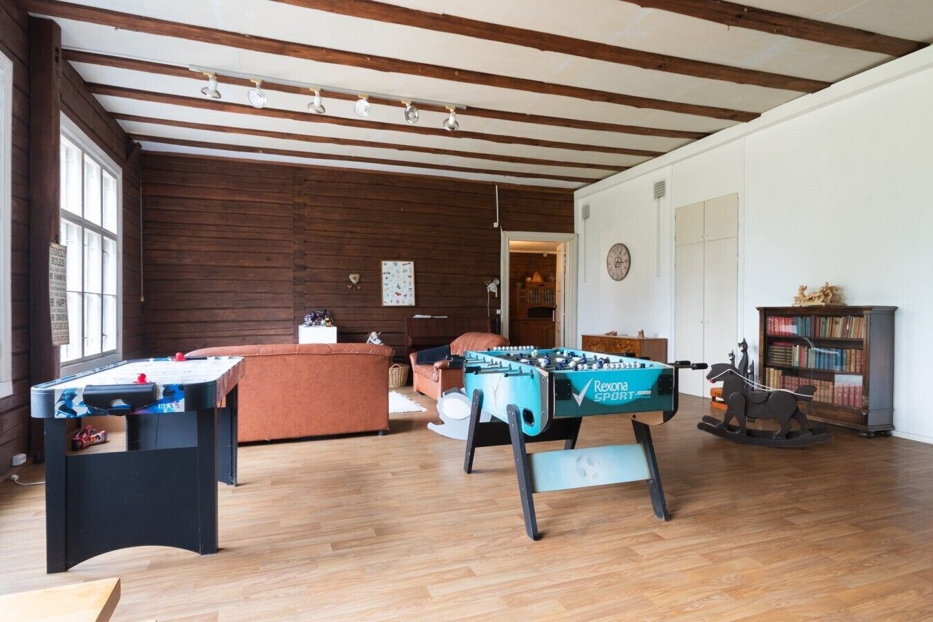 Una habitación amplia con vigas de madera en el techo, una mesa de fútbol de mesa, una mesa de billar y un sofá.
