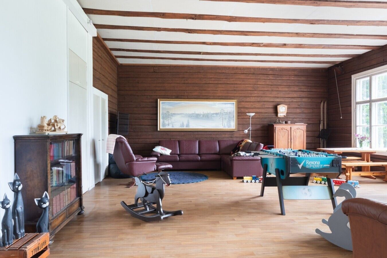 Una sala de estar acogedora con techo de madera, un sofá, un sillón mecededor, una mesa de fútbol y una estantería.