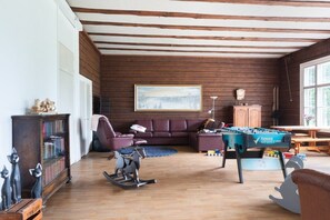 A cozy living room with a wooden ceiling, a sofa, a rocking chair, a foosball table, and a bookshelf.