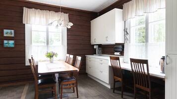 A wooden-paneled room with a dining table, chairs, a kitchen area with cabinets, and a window with curtains.
