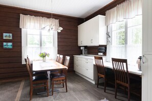 Quarto com painéis de madeira, mesa de jantar, cadeiras, área de cozinha com armários e janela com cortinas.