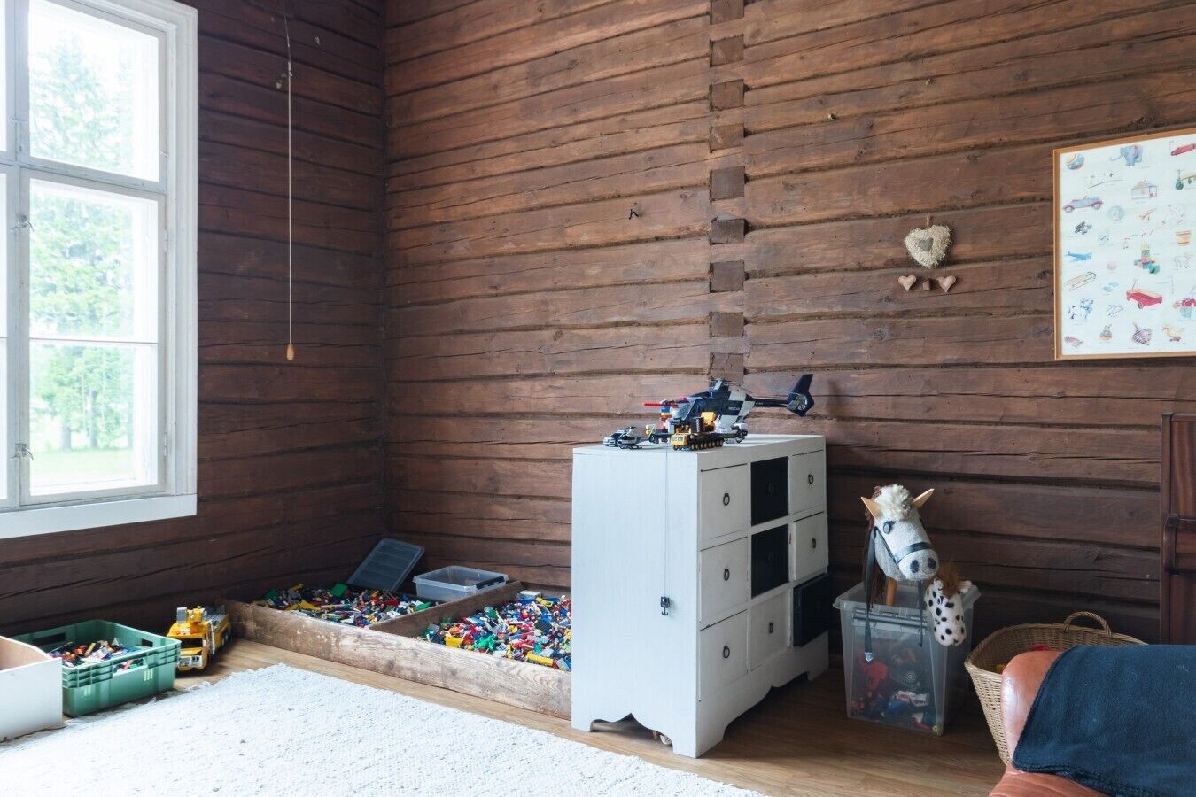 A room with wooden walls, a window, a play area with toys, a white dresser, and a toy horse.