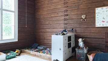 A room with wooden walls, a window, a play area with toys, a white dresser, and a toy horse.