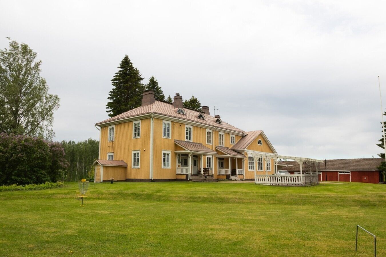 A large two-story building with a porch and a fenced garden area.