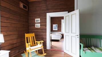 A wooden room with a rocking chair, a bed, and a door leading to another room.