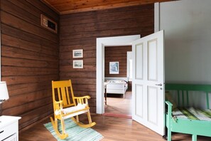 A wooden room with a rocking chair, a bed, and a door leading to another room. - Historic countryside schoolhouse for gatherings, retreats & celebrations (Hartola)