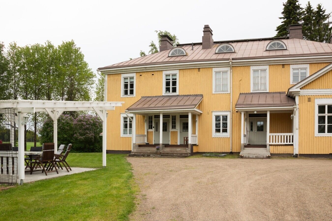 Kaksikerroksinen keltainen rakennus, jossa on katettu kuisti ja sorapäällysteinen ajotie.