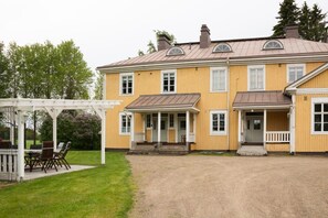 A two-story yellow building with a covered porch and a gravel driveway.