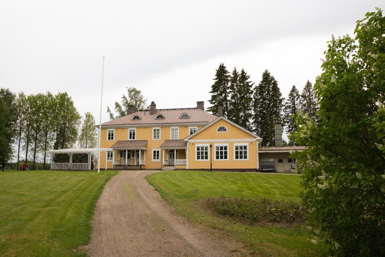 Kaksikerroksinen keltainen talo, jossa on katettu kuisti ja sorapäällysteinen ajotie.