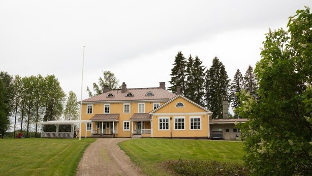 Ein gelbes, zweistöckiges Haus mit überdachter Veranda und Kiesweg.