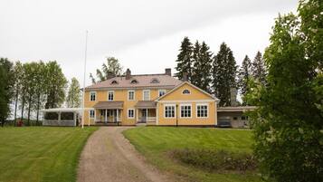 Kaksikerroksinen keltainen talo, jossa on katettu kuisti ja sorapäällysteinen ajotie.
