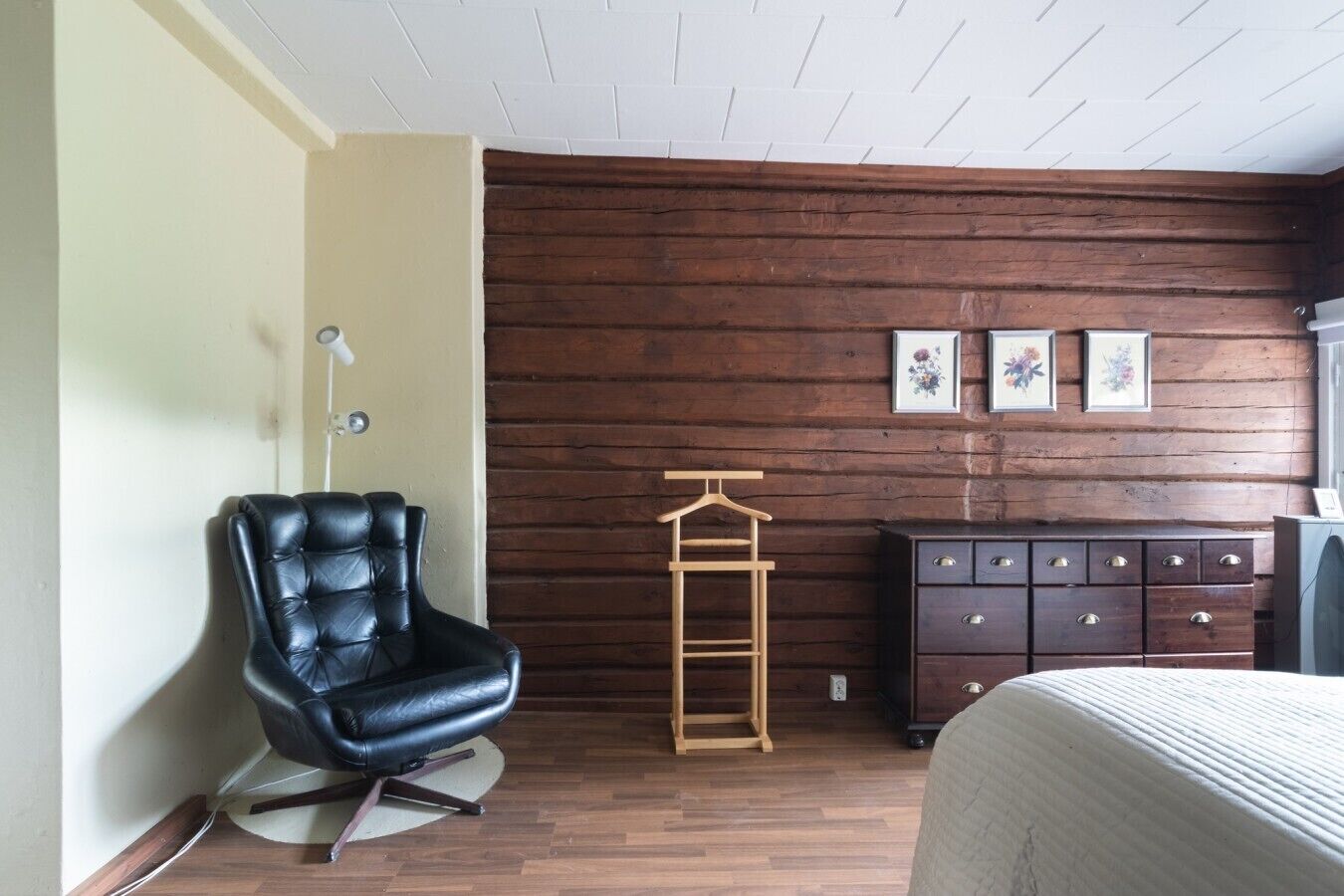 A room with a black leather chair, a wooden dresser, and a bed.