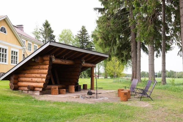 A log cabin with a sloped roof and a covered porch. There are two chairs and a table outside.