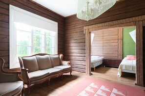 A room with a wooden slatted ceiling, a sofa, a bed with a green headboard, and a chandelier. - Historic countryside schoolhouse for gatherings, retreats & celebrations (Hartola)