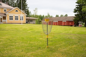 A disc golf basket on a grassy field with houses in the background.