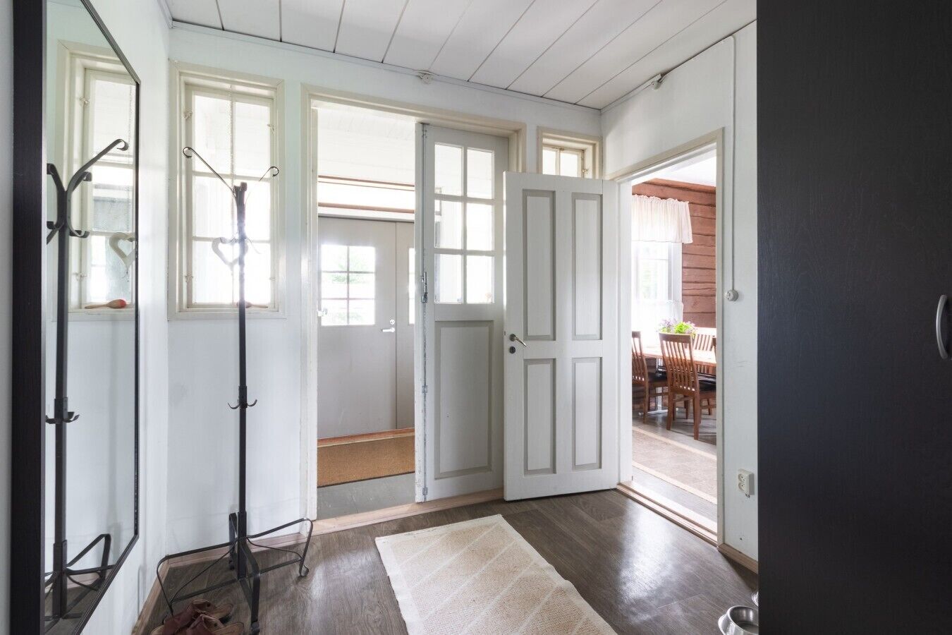 A room with a wooden floor, a white door, and a view of an outdoor dining area.