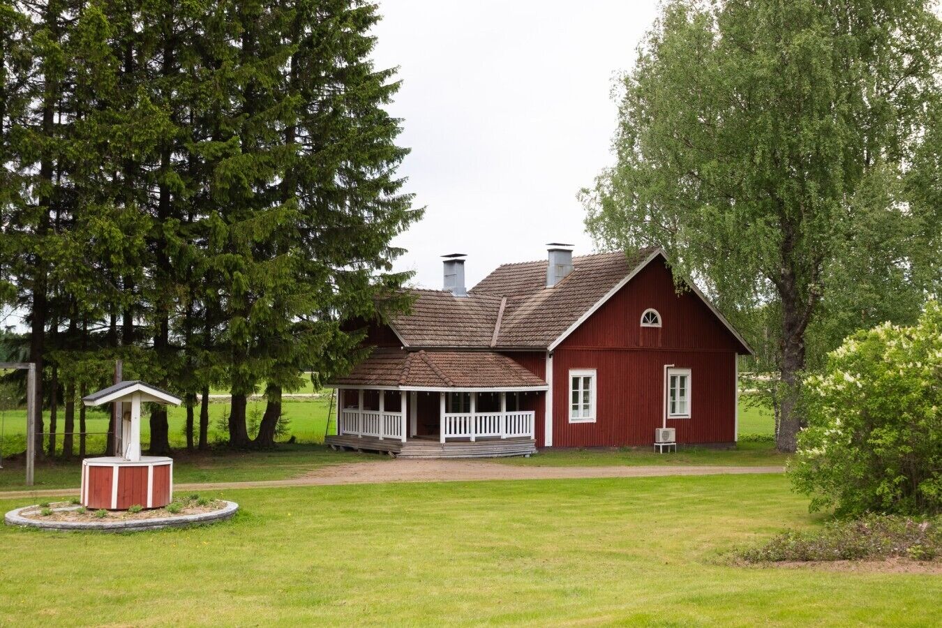 A red barn with a porch, surrounded by trees and a grassy field.