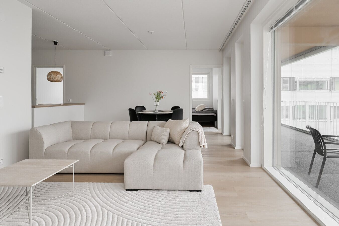 A modern living room with a sectional sofa, a dining table with chairs, and a view through large windows.