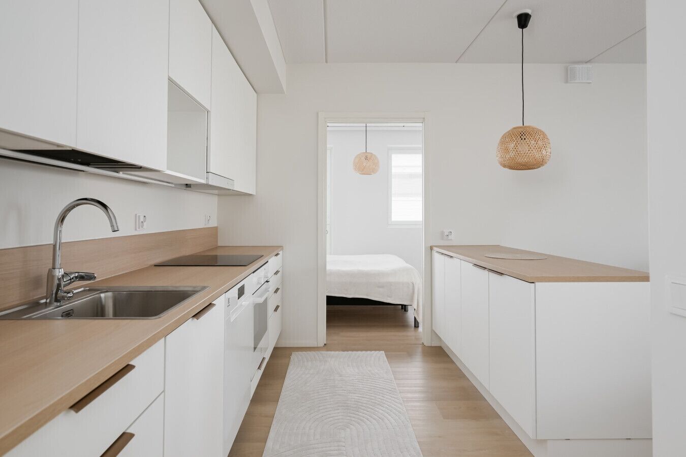 A modern kitchen with white cabinetry, a wooden countertop, and a stainless steel sink.