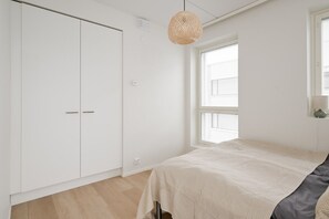A bedroom with a bed, a wardrobe, a window with blinds, and a hanging light fixture. - Family apartment with great views of Jyväskylä city (Jyväskylä)