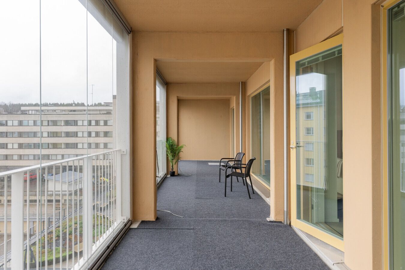 A balcony with a view of a building, a potted plant, and two chairs.